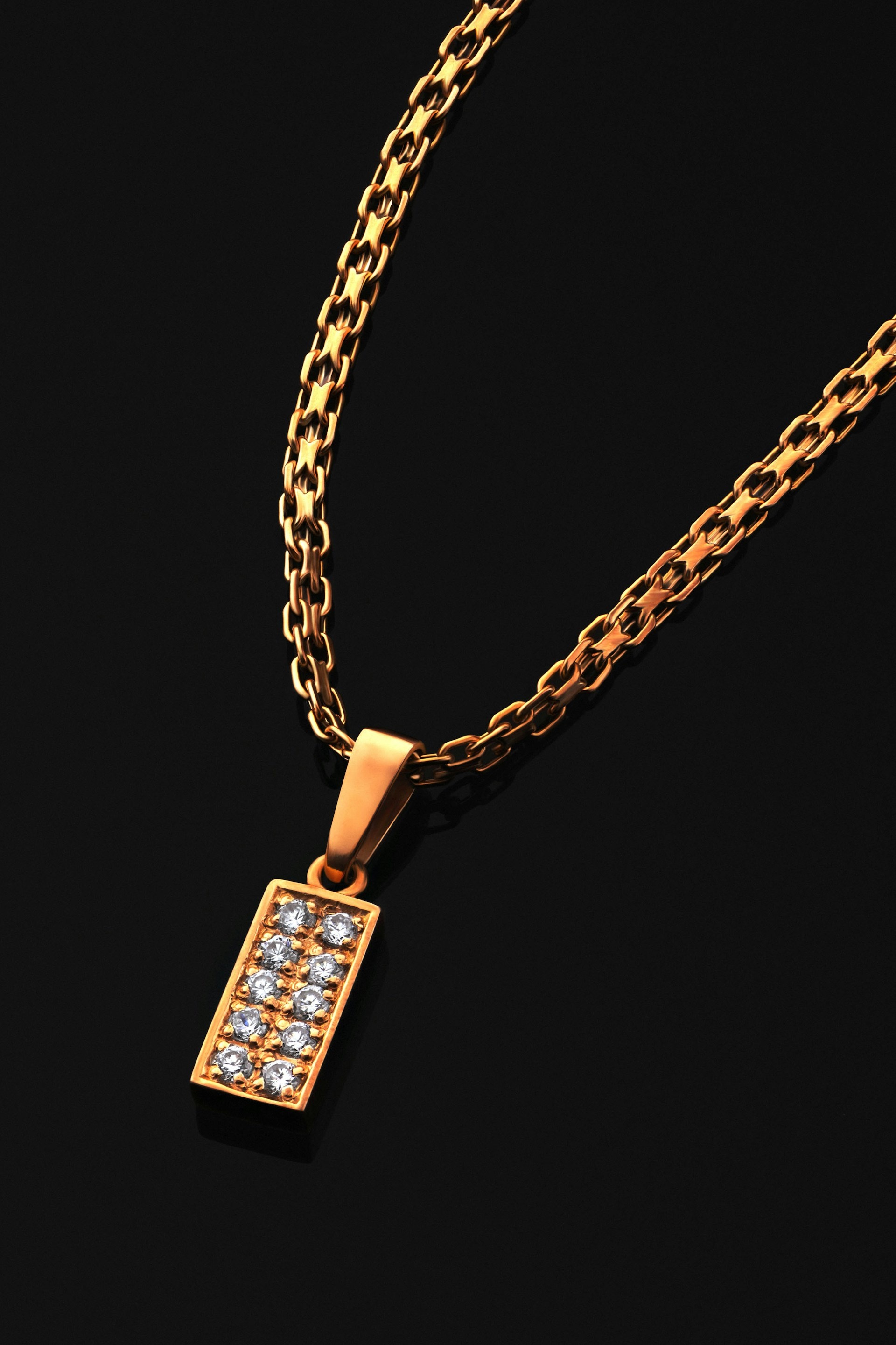 Gold necklace with rectangular diamond pendant on dark surface, elegant rim light
