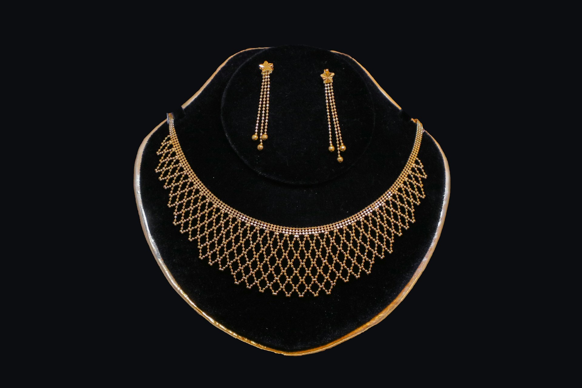 Gold earrings and necklace set displayed on black velvet, woven design
