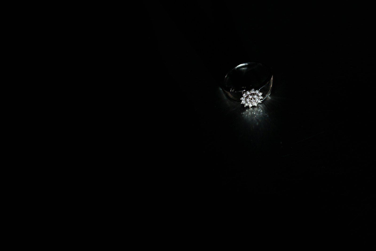 Diamond ring on dark velvet, single spotlight creating dramatic pool of light