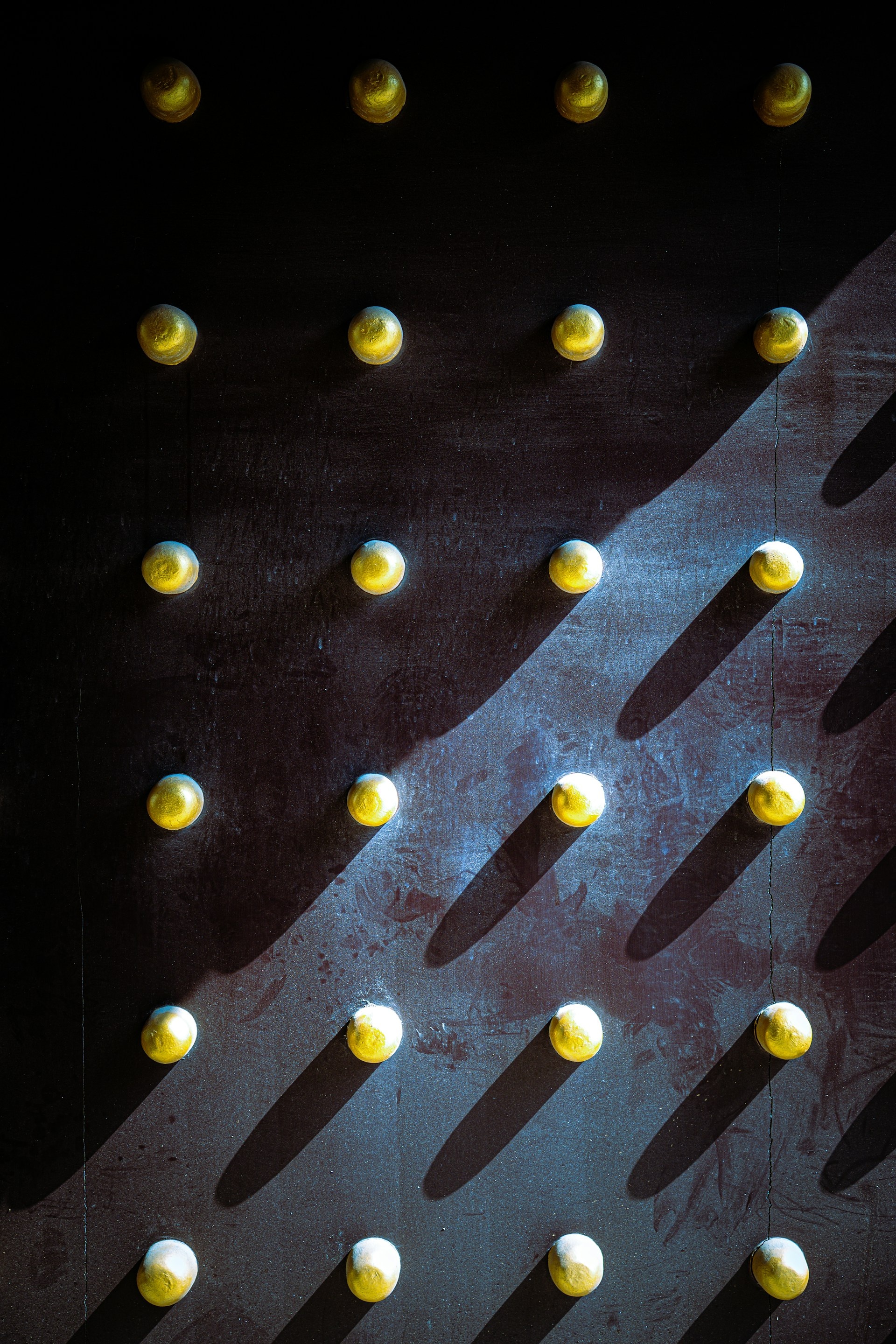 Rows of warm golden studs casting soft shadows on dark surface, evoking heritage craftsmanship