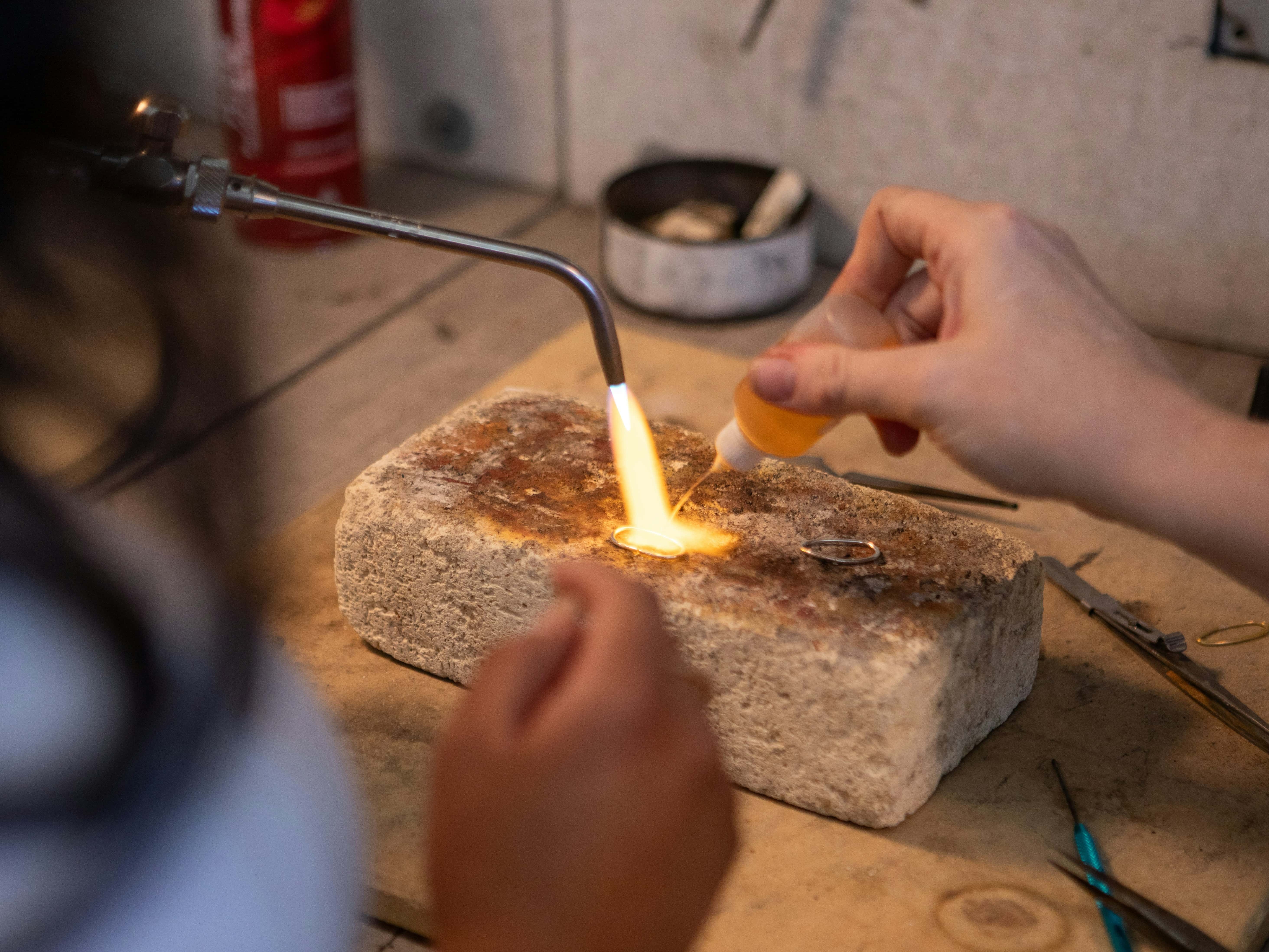 Jeweler using a torch to heat metal on a workbench, warm fire glow